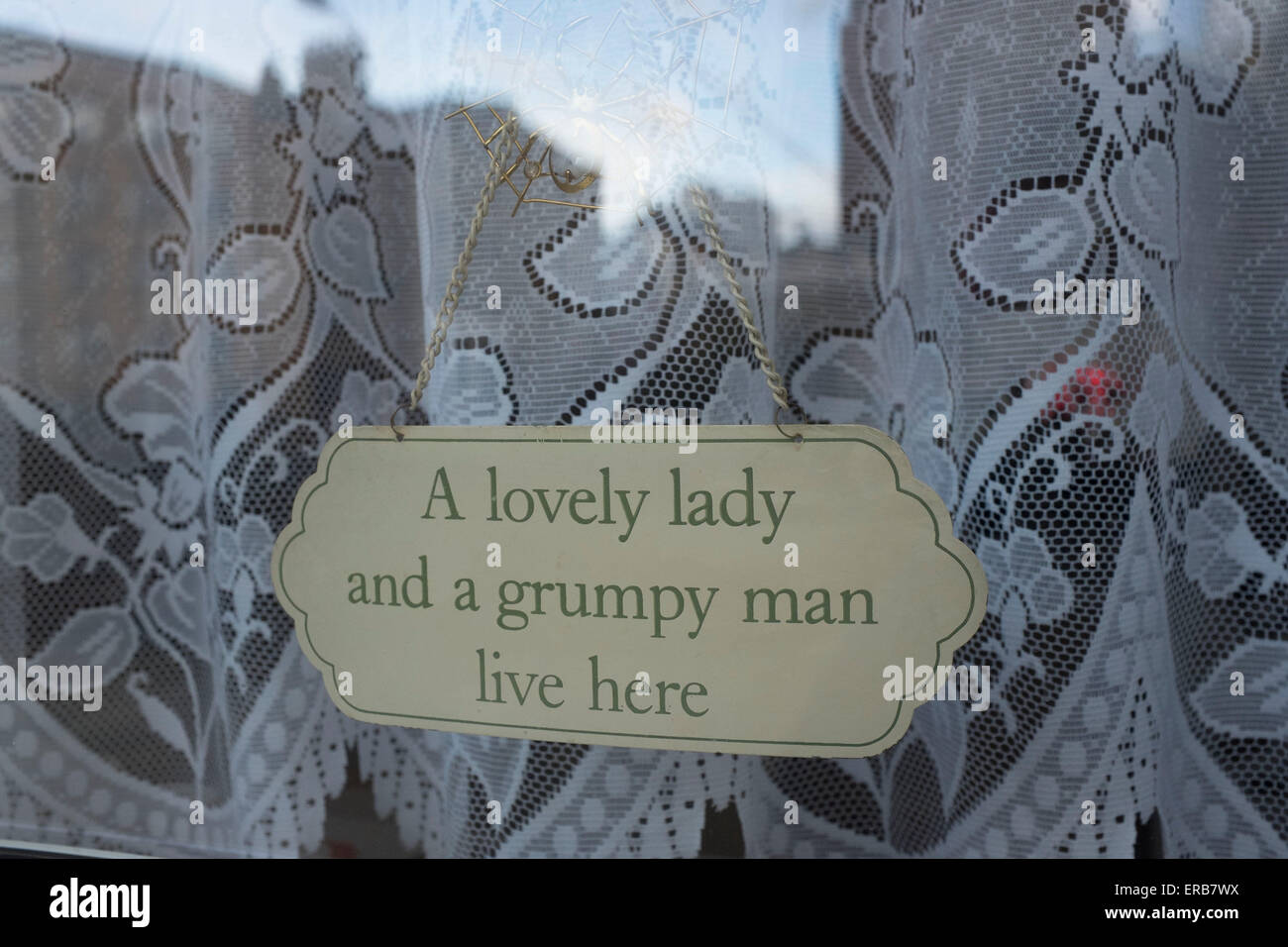 A lovely lady and a grumpy man live here. Sign in a living room front window filled with net curtains of a council flat in South Stock Photo