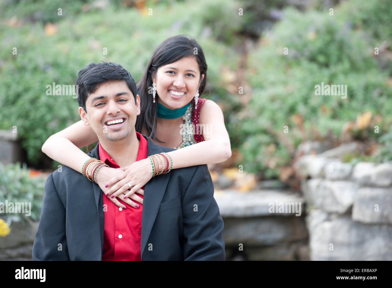 A young and happy Indian couple posing near a pile of rocks on a cloudy ...