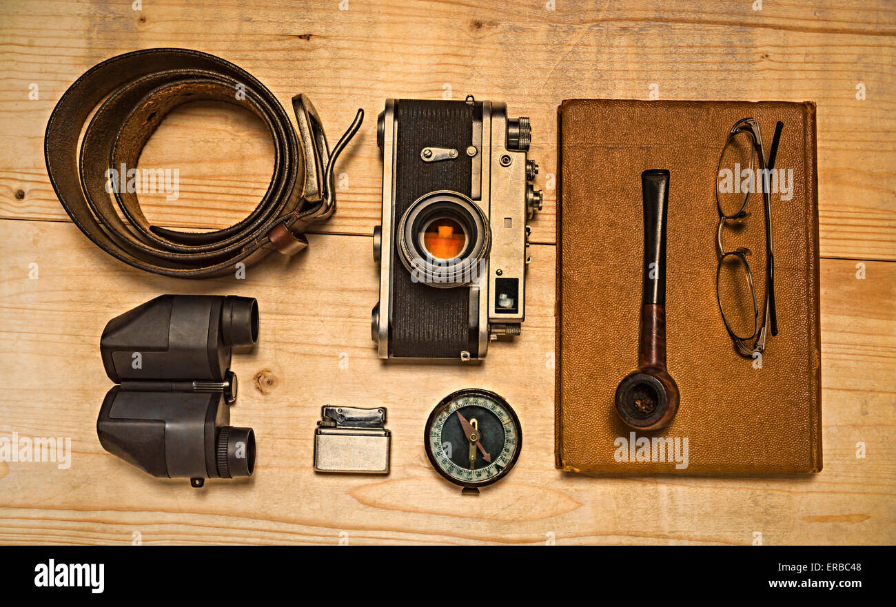 Still life with retro object. Book with compact old camera, compass, cigarette lighter, belt, glasses, pipe, binocular on table Stock Photo