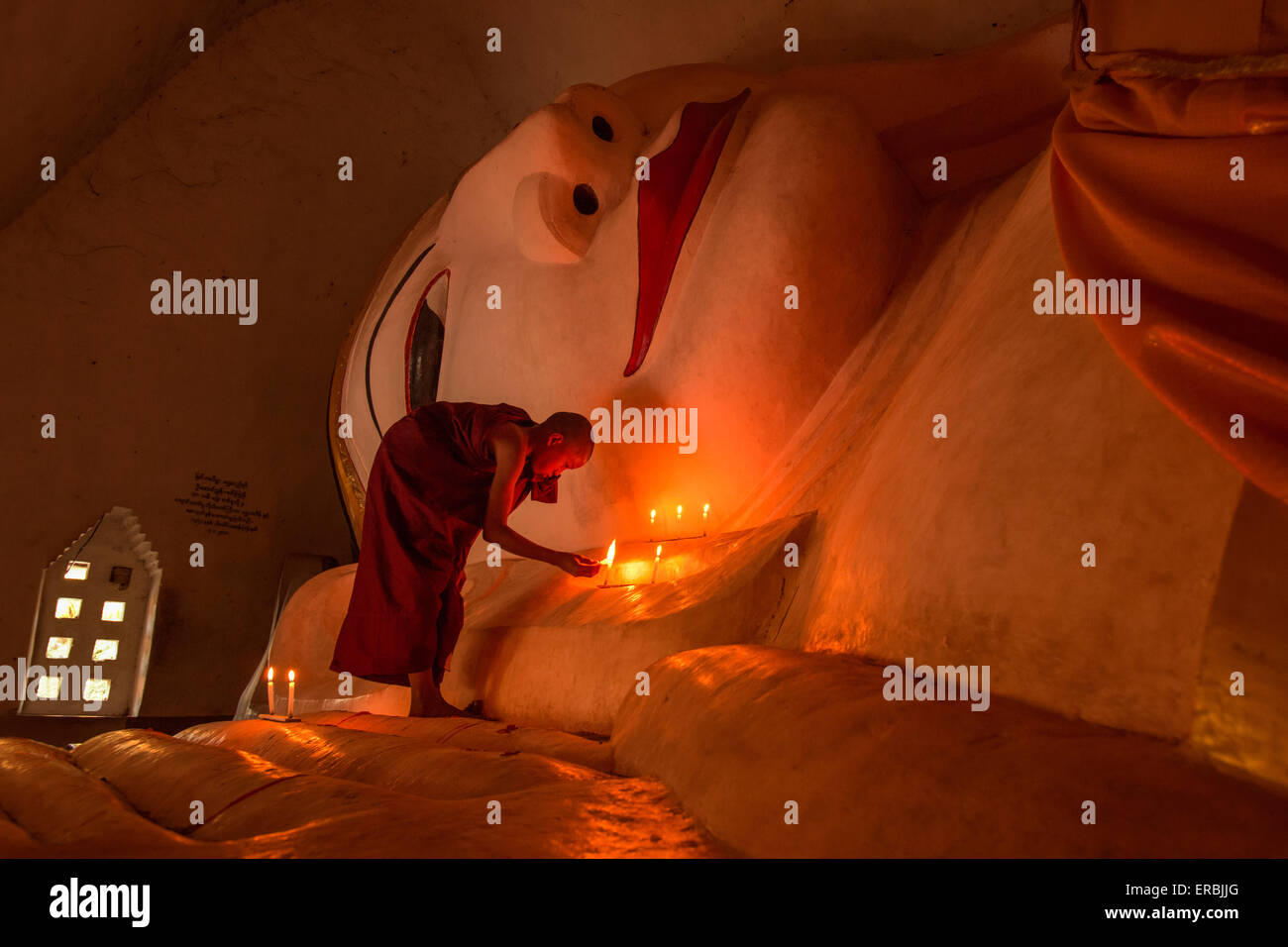 Monk lighting candles at reclining Buddha in Mandalay Myanmar Stock Photo