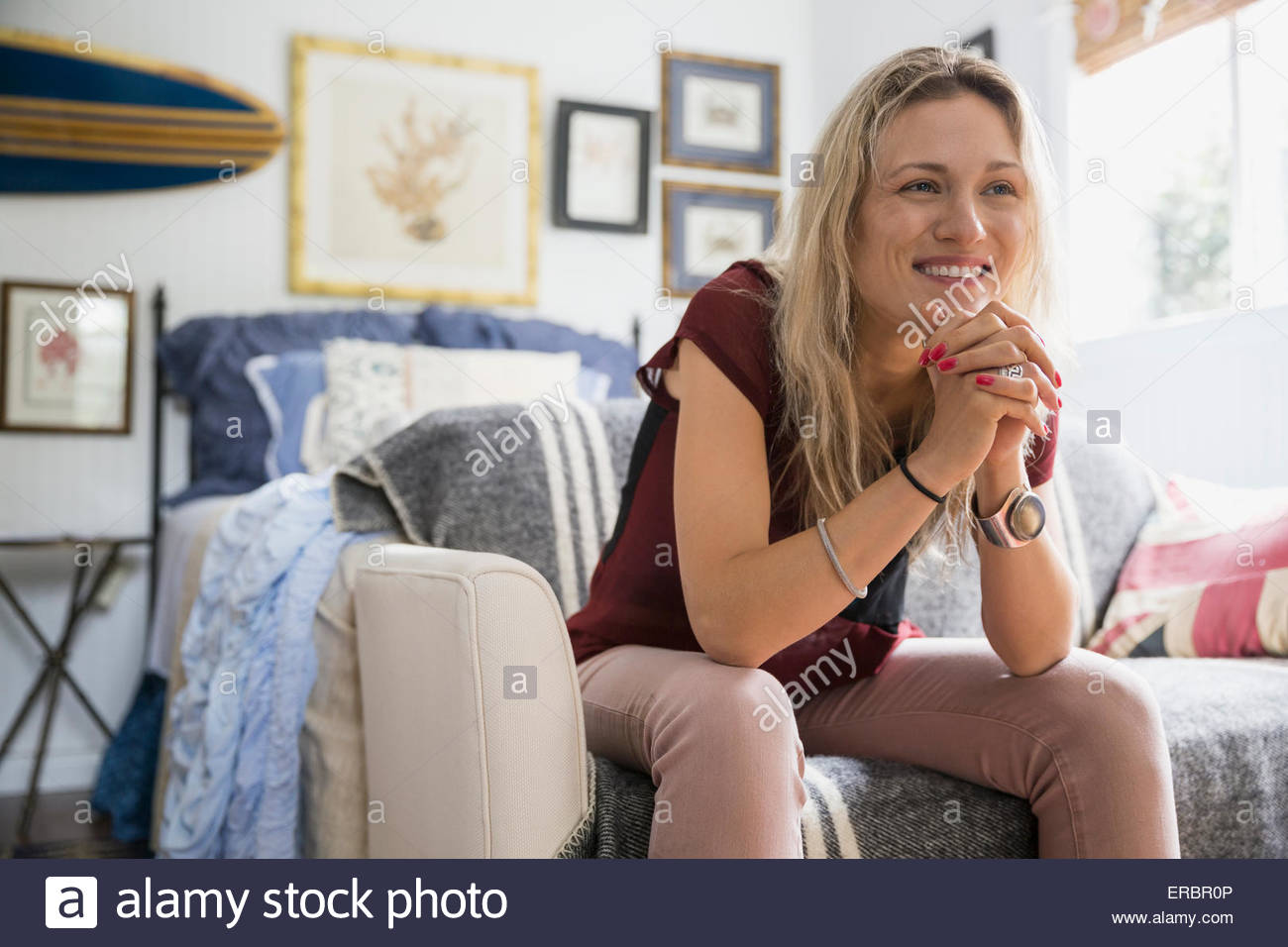 Smiling blonde woman with hands clasped on sofa Stock Photo