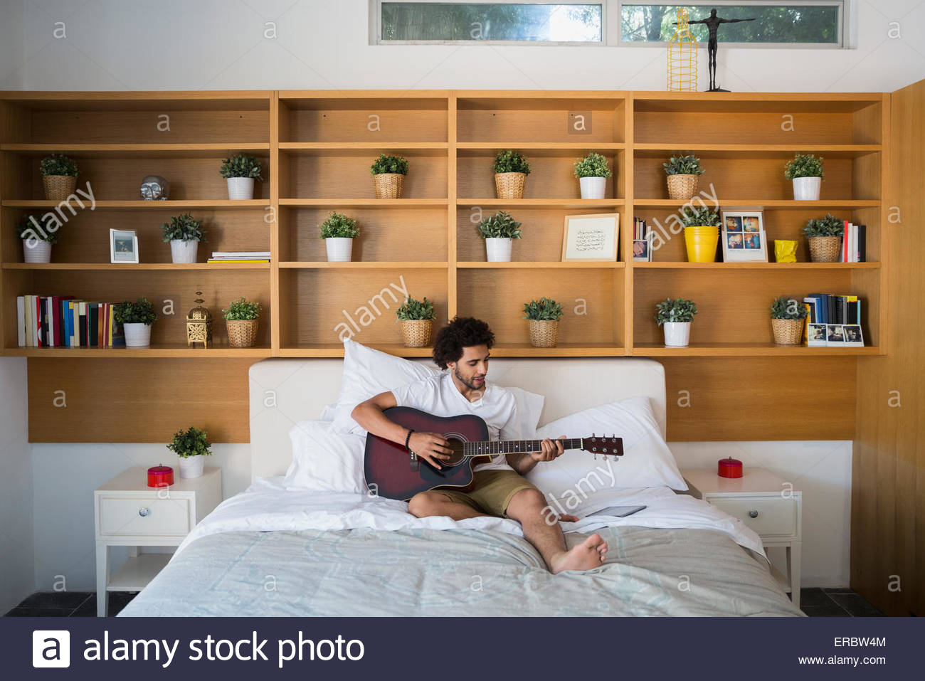Man playing guitar on bed in bedroom Stock Photo Alamy