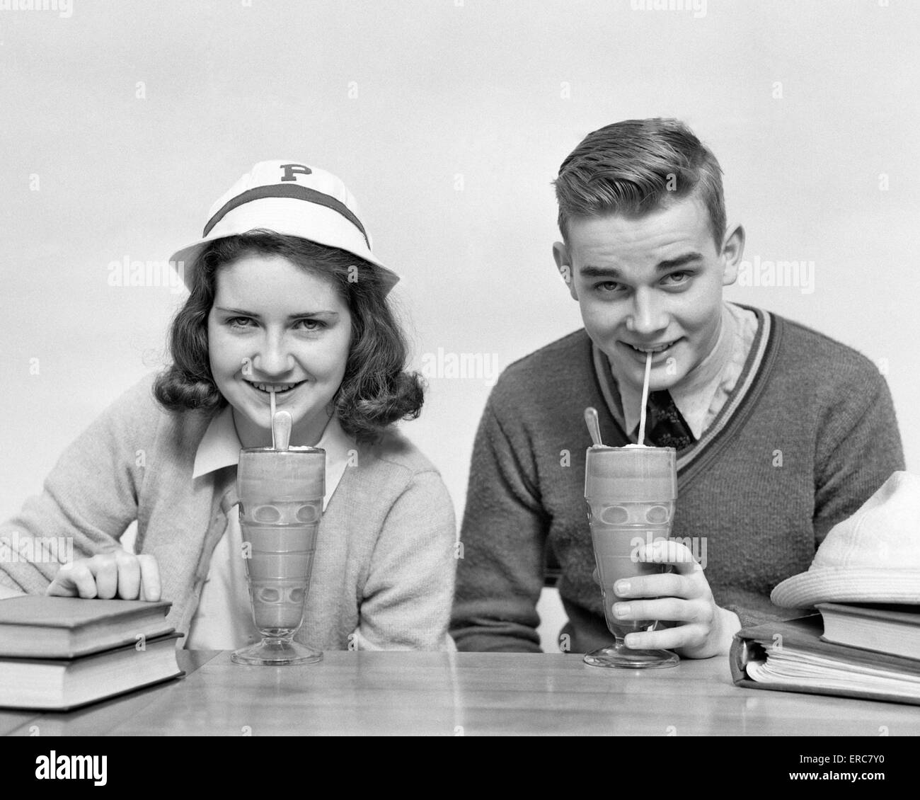 1940s TEENAGE BOY AND GIRL DRINKING MILKSHAKES TOGETHER LOOKING AT CAMERA Stock Photo