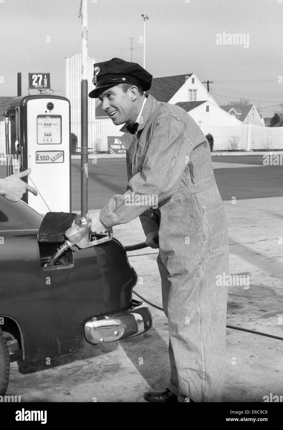 1950s SERVICE STATION ATTENDANT MAN IN STRIPED OVERALLS & CAP FILLING GAS TANK OF AUTOMOBILE Stock Photo
