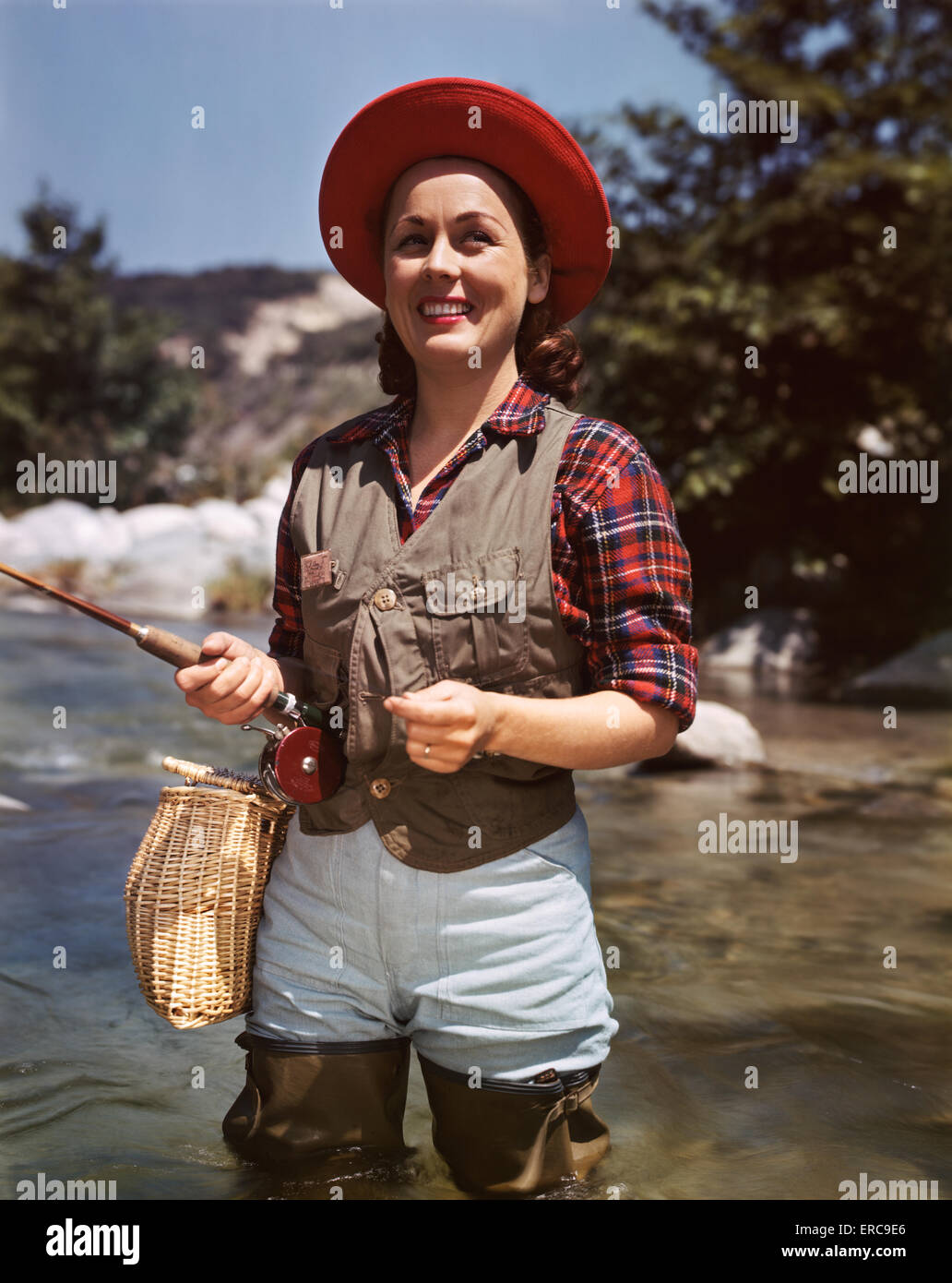 1940s 1950s SMILING WOMAN STANDING IN STREAM FLY FISHING WEARING