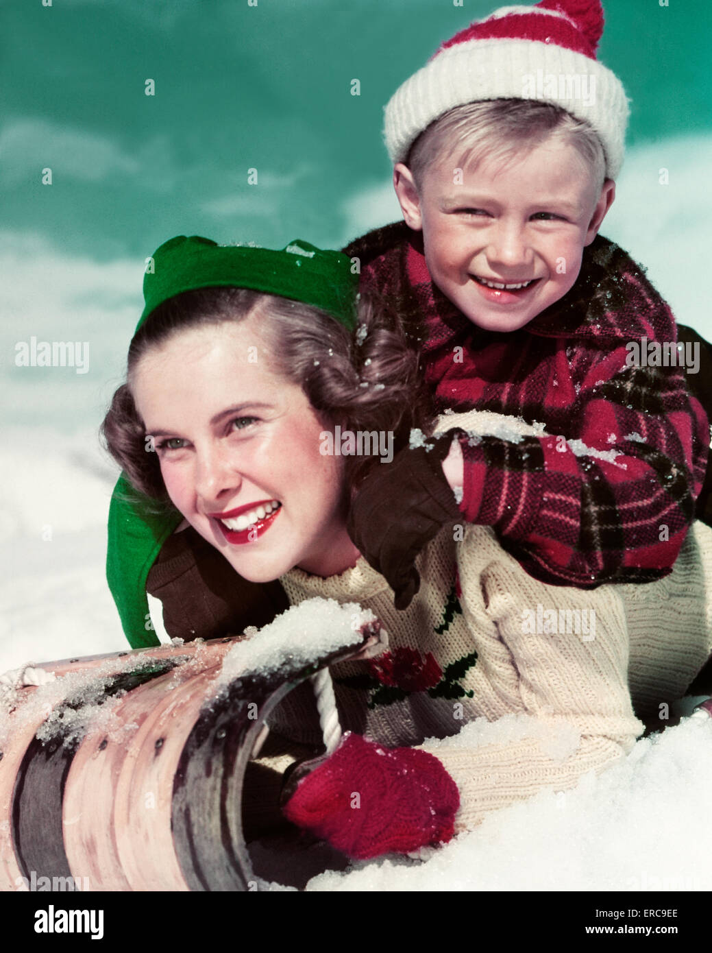 1940s 1950s SMILING TEENAGE GIRL SISTER AND YOUNGER BOY BROTHER LOOKING AT CAMERA RIDING TOBOGGAN DOWNHILL Stock Photo