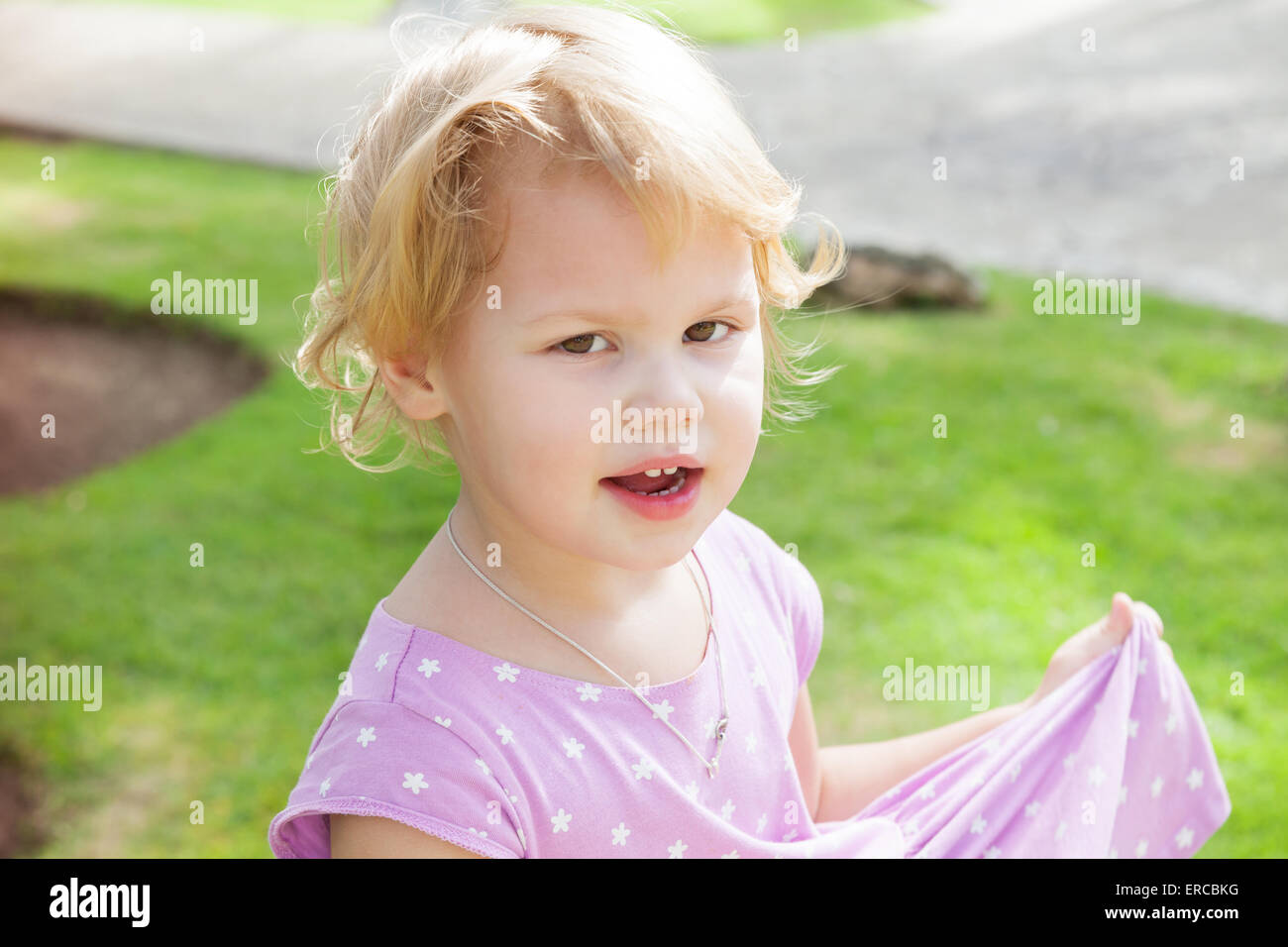 Outdoor portrait of cute smiling Caucasian blond baby girl in a summer ...