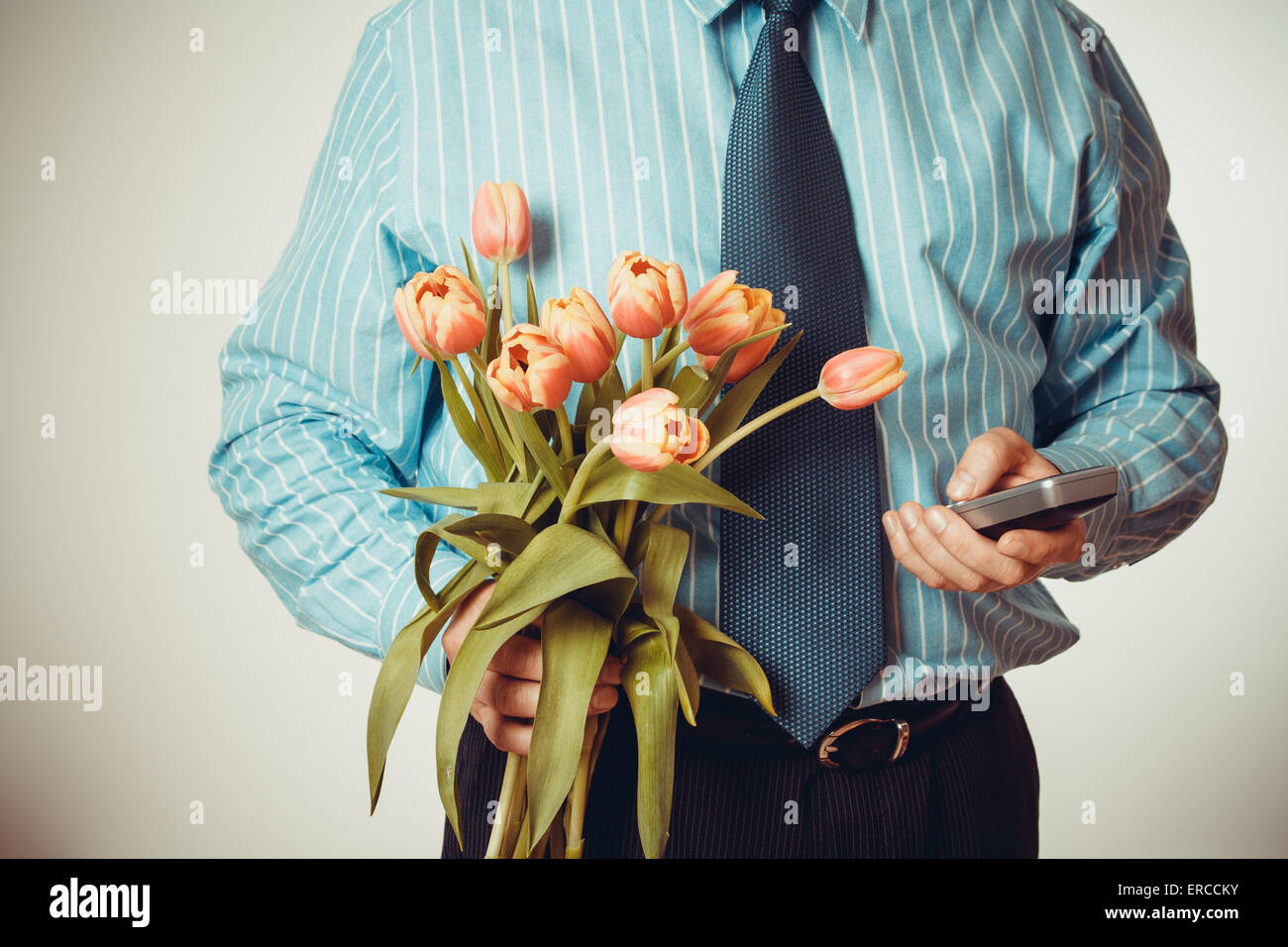 Businessman dials phone number, holding tulips, half body, vignette style Stock Photo