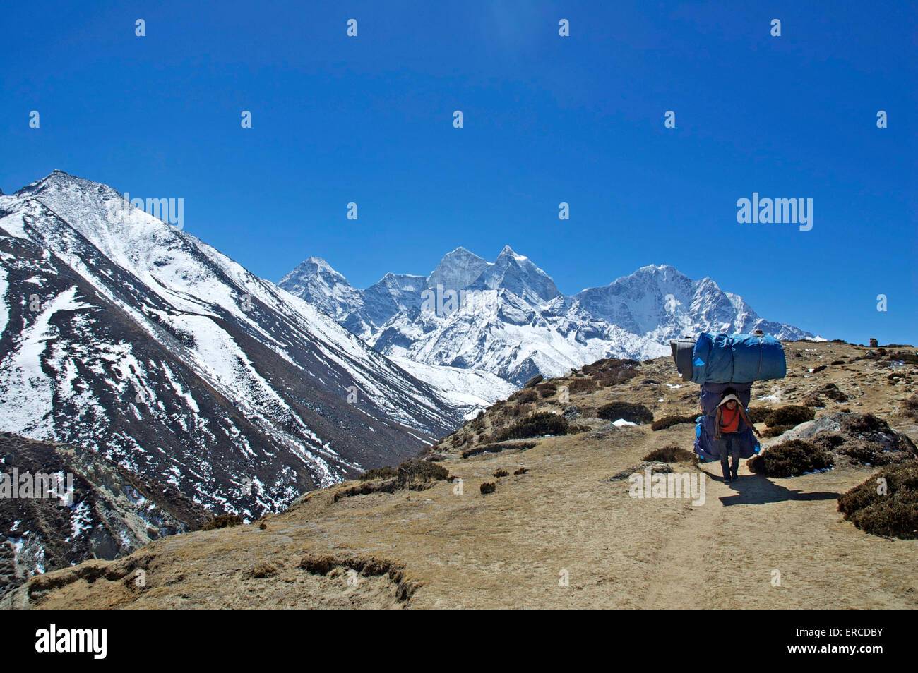 A heavily laden porter traverses a hill on the Everest trail in the Nepali Himalayas Stock Photo