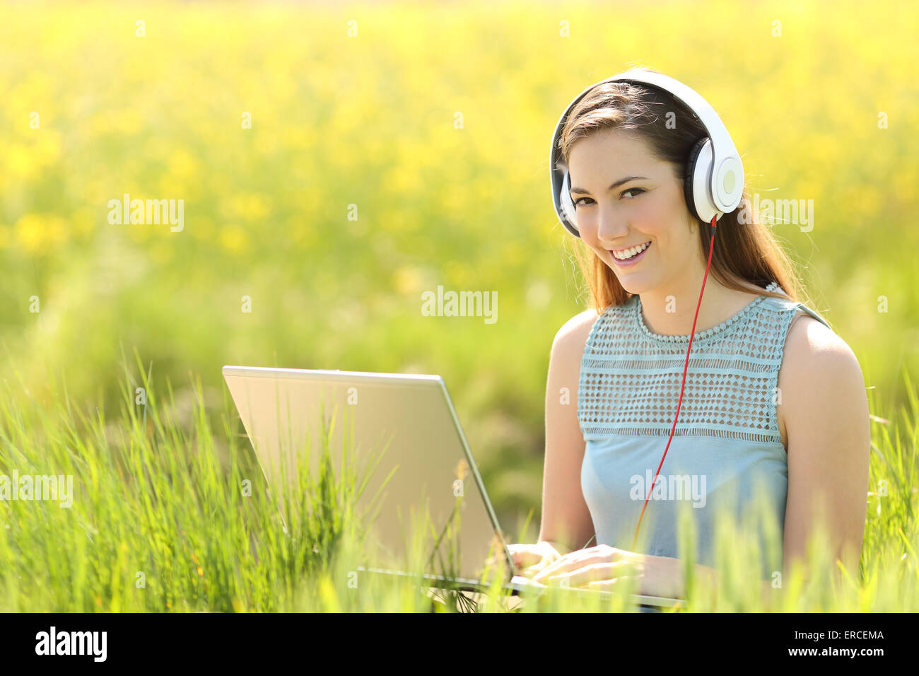 Woman working with a laptop and headphones in a field looking at camera Stock Photo