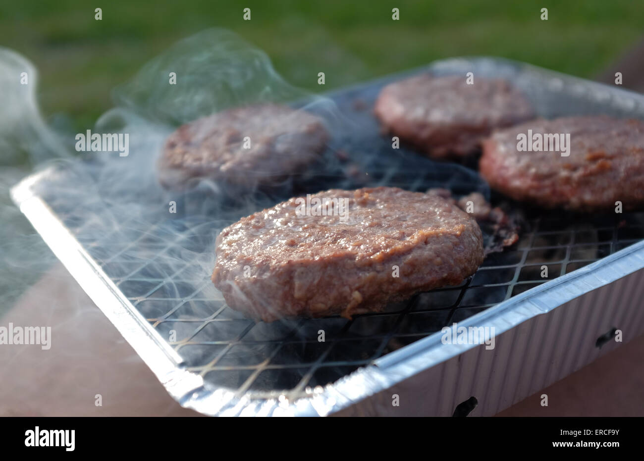 Burgers cooking on a disposable barbecue BBQ Stock Photo