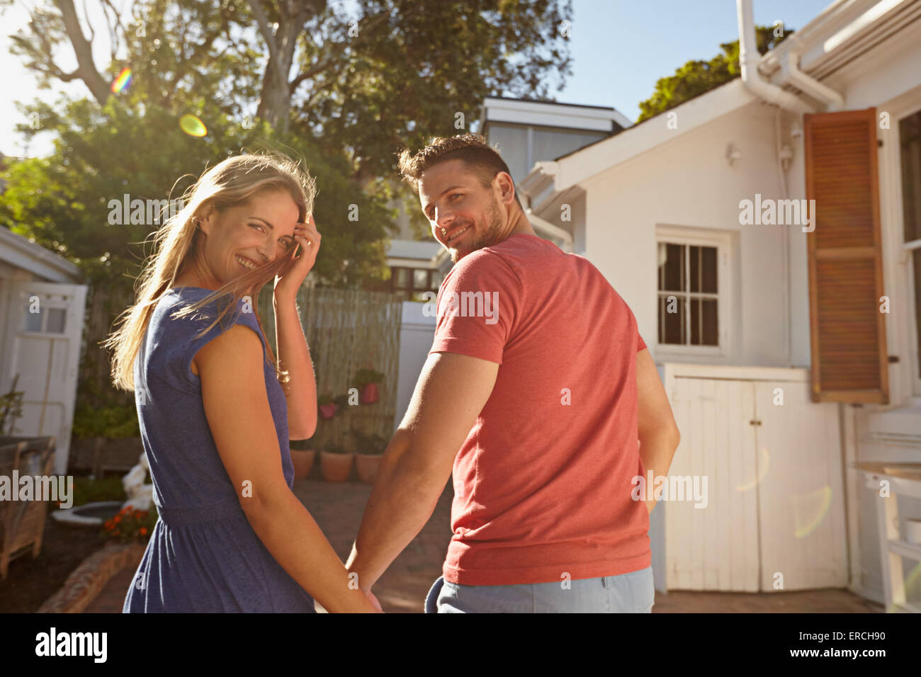Rear view shot of a young couple taking a walk around their house holding hands. Loving young couple outdoors in their backyard Stock Photo