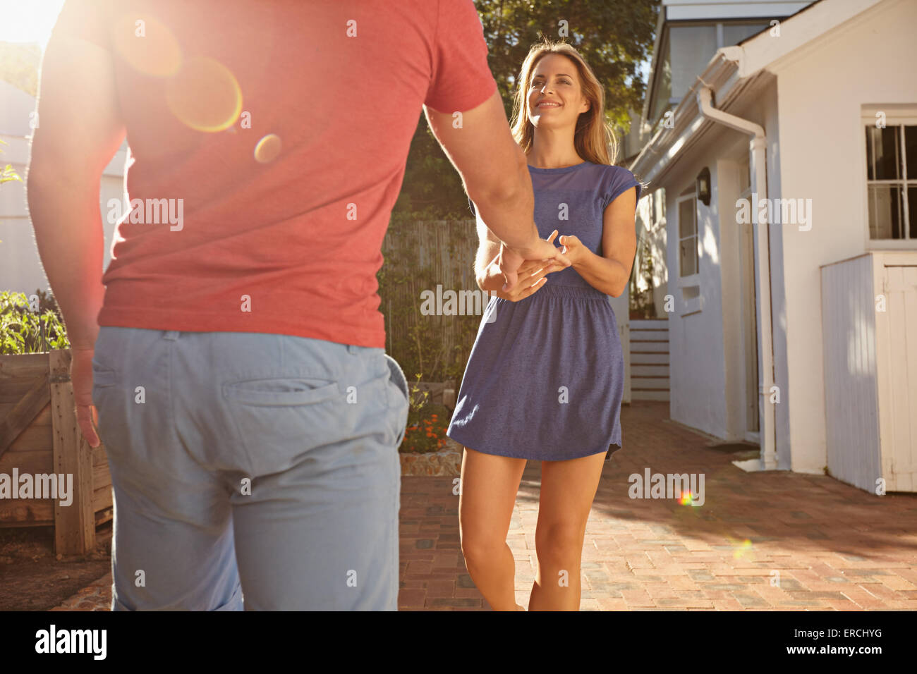 Couple outside their home with young woman pulling her boyfriend. Young woman holding hand of her boyfriend while talking in the Stock Photo