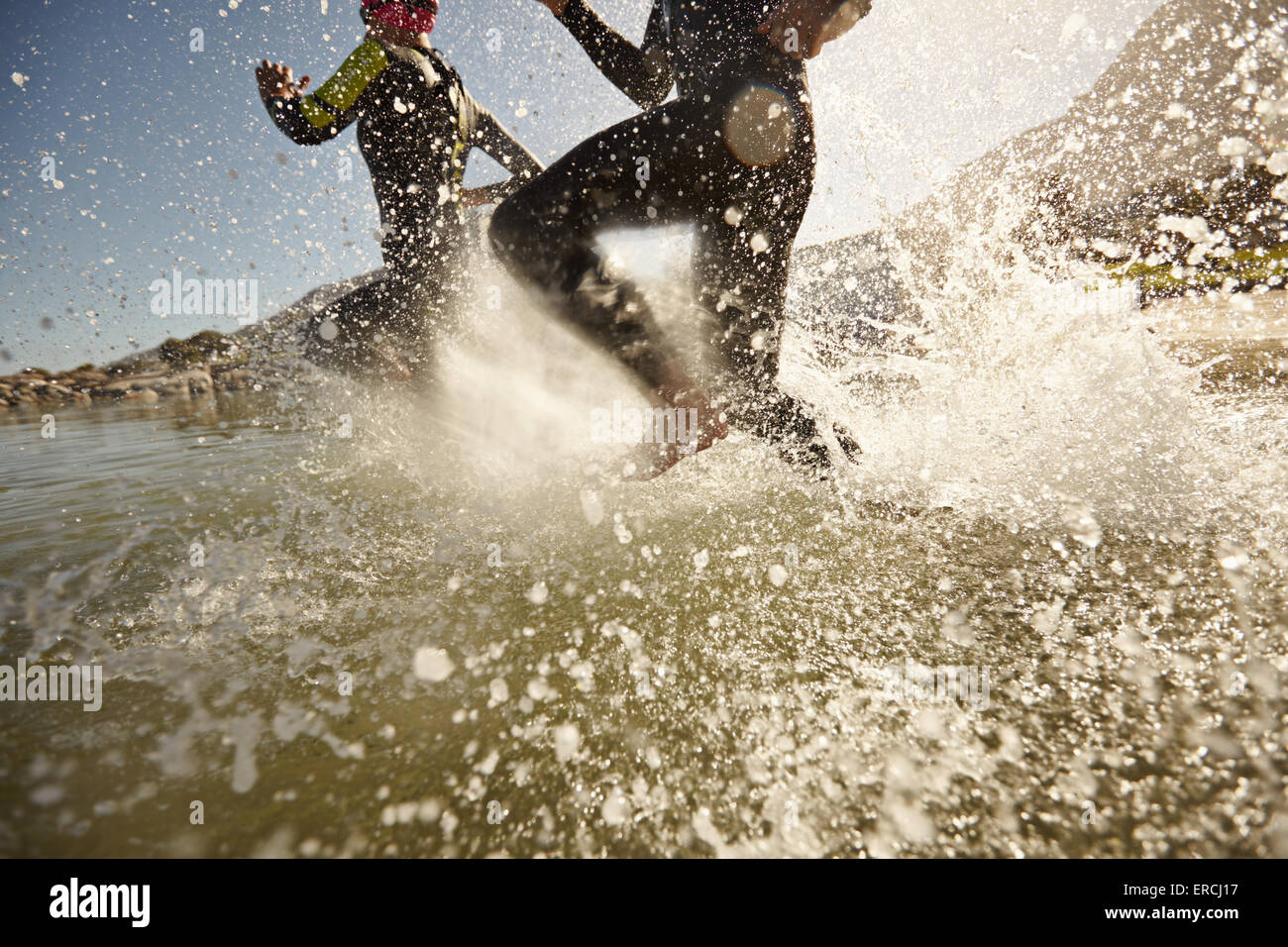 Two triathlon participants running into the water for swim portion of race. Splash of water and athletes running. Focus on water Stock Photo