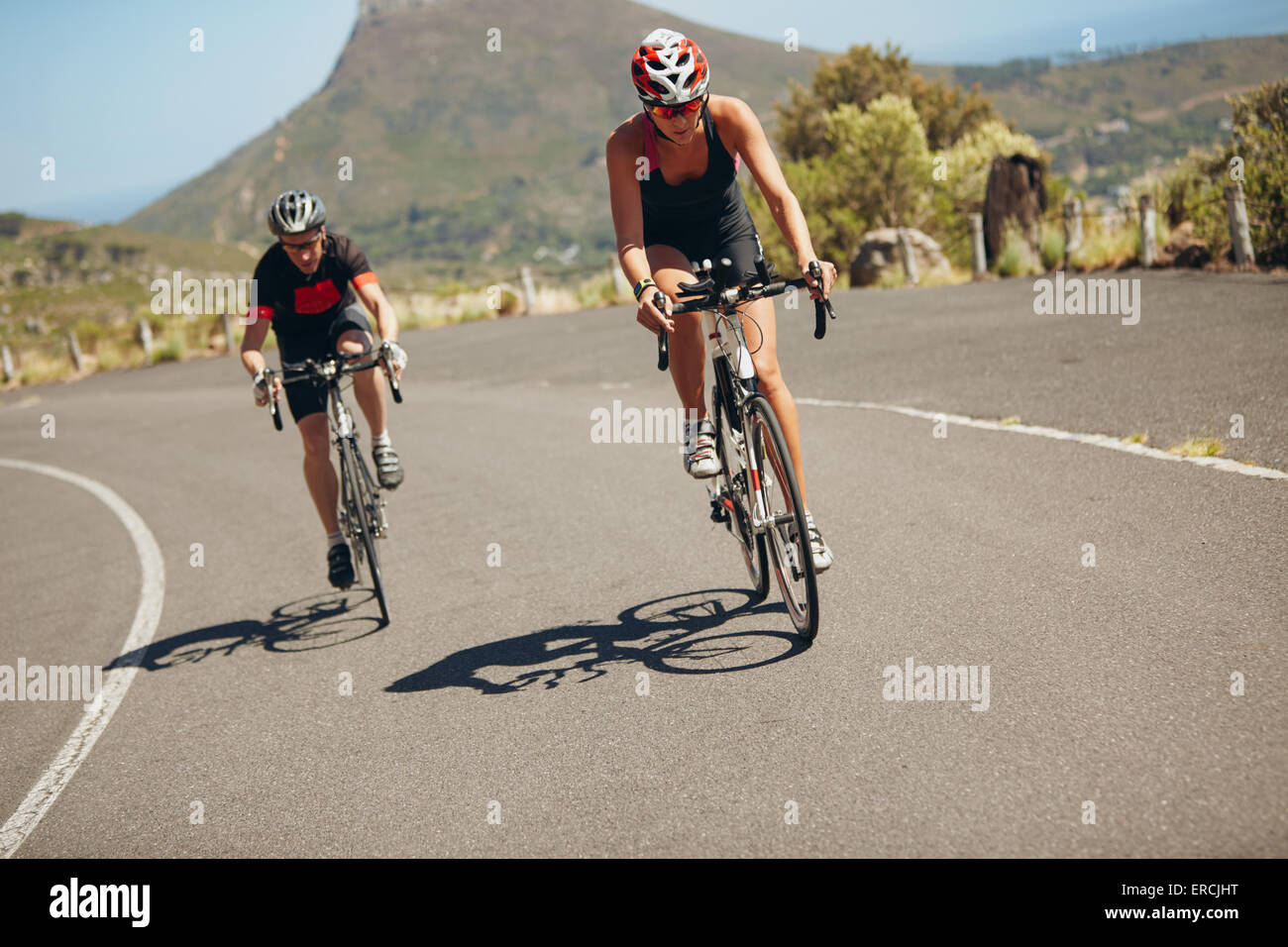 Cyclist riding bikes on open road. Triathletes cycling down the hill on bicycles. Practicing for triathlon race on country road. Stock Photo