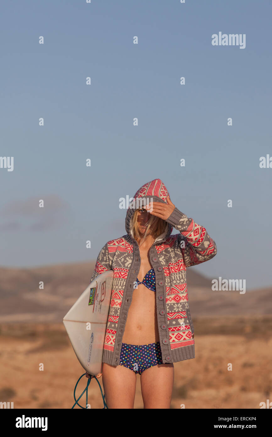 Surfer girl in bikini wearing a hoodie with her board on the beach at  sunset Stock Photo - Alamy