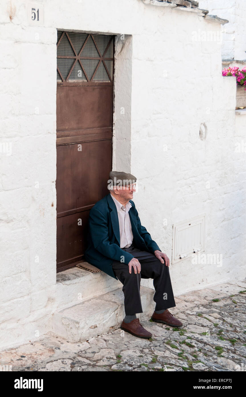 Old Man Sits and Relaxes in front of Trullo House, Alberobello, Puglia, Italy Stock Photo