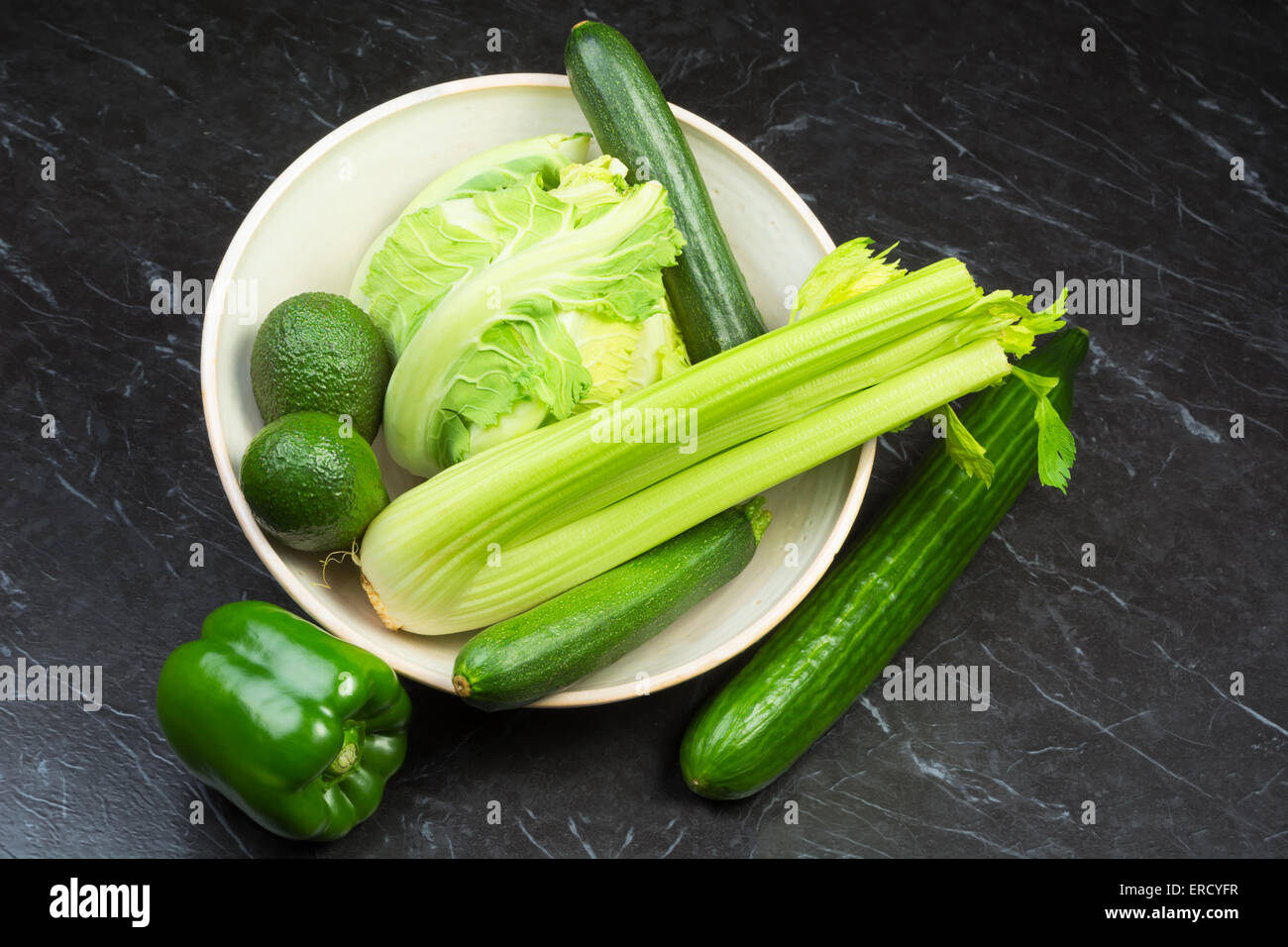 Assorted fresh green vegetables in a ceramic bowl on a black stone surface Stock Photo