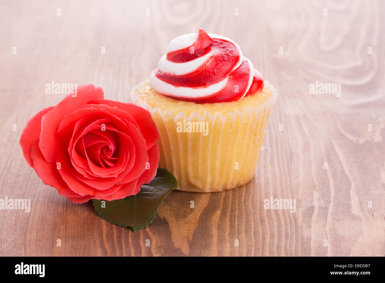 Strawberry cupcake with a beautiful red rose on wooden table, a simple treat to a loved one Stock Photo