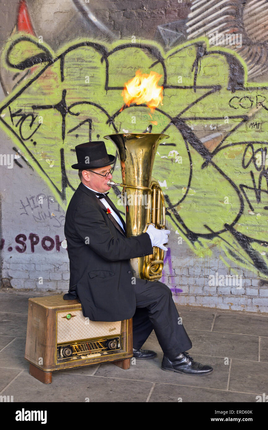 street performer sitting on old radiogram playing Tuba with flame coming out  in London United Kingdom Stock Photo