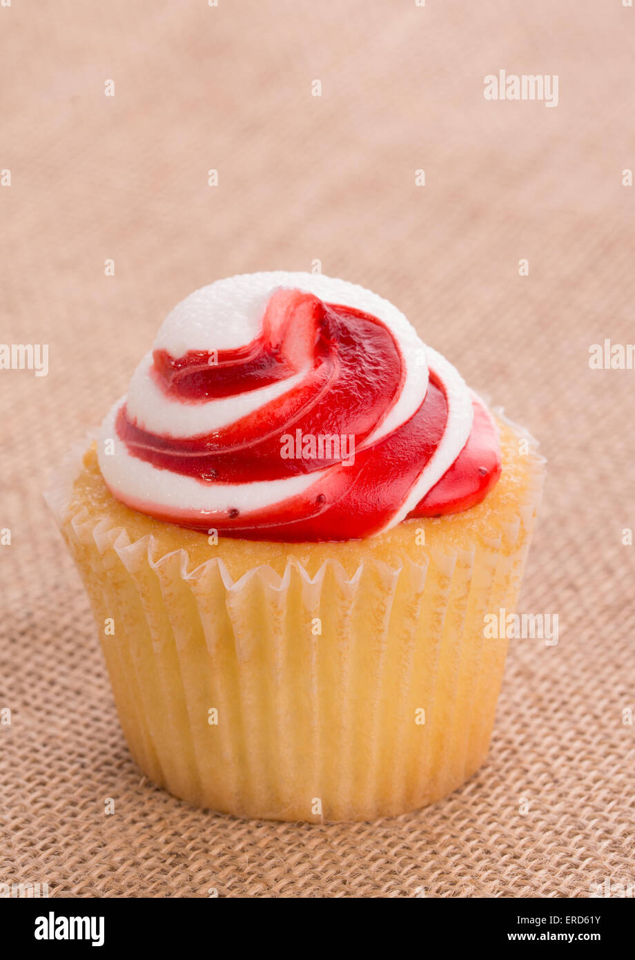 Strawberry flavored swirly top cupcake on simple burlap background Stock Photo