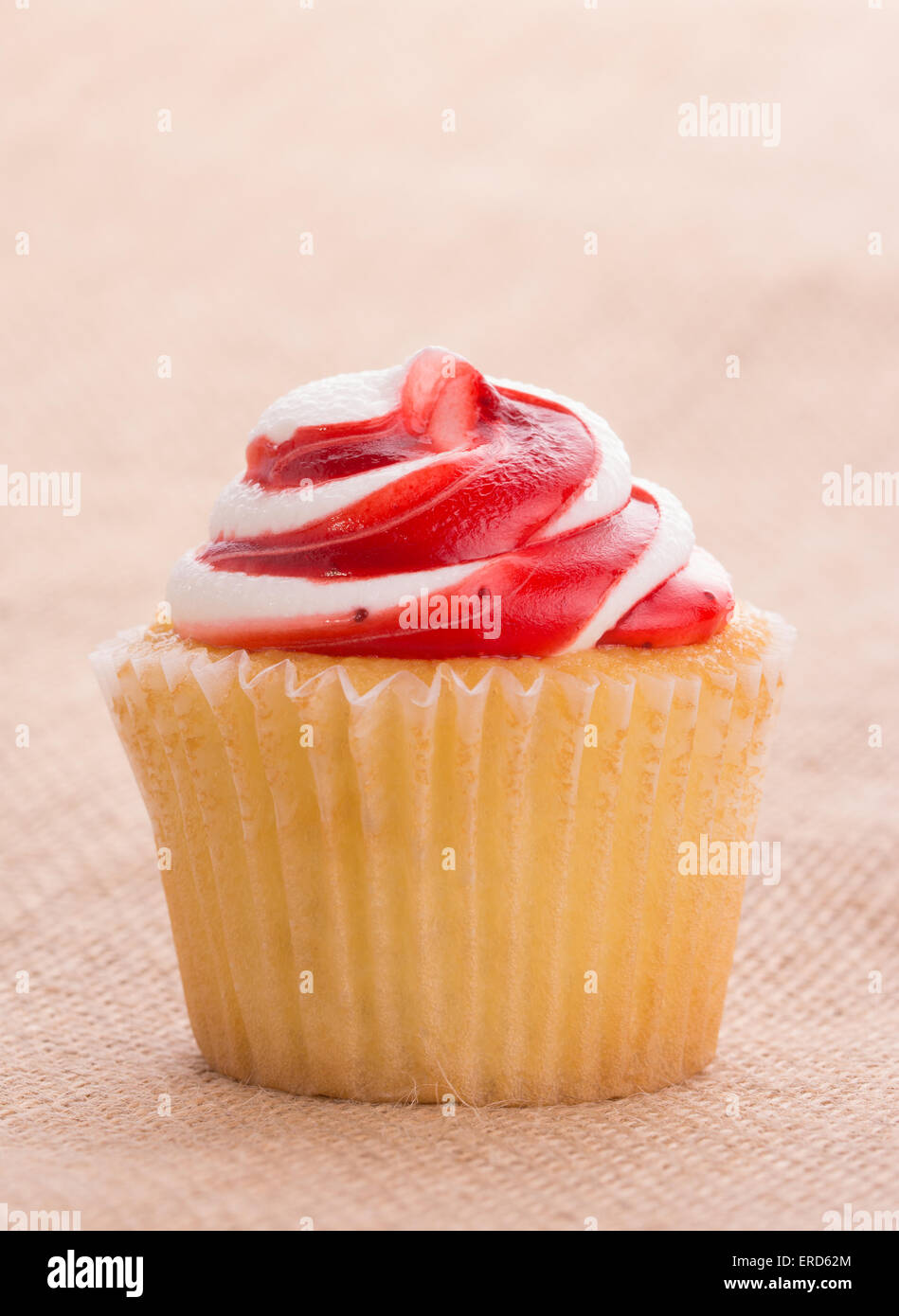 Delicious red and white swirly top strawberry cupcake on simple burlap background Stock Photo