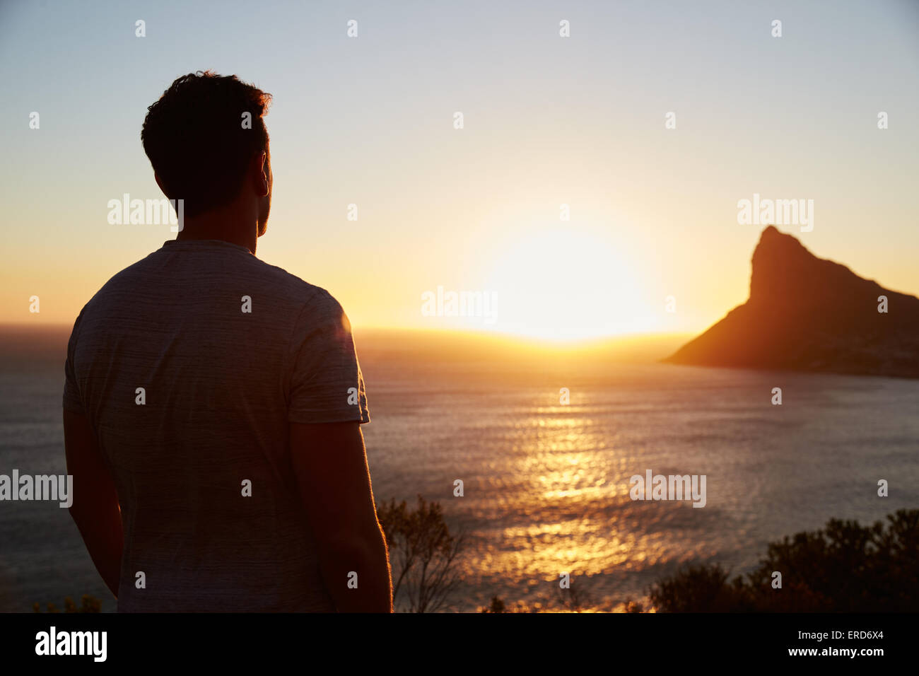 Silhouette Of Man Watching Sun Set Over Sea And Cliffs Stock Photo