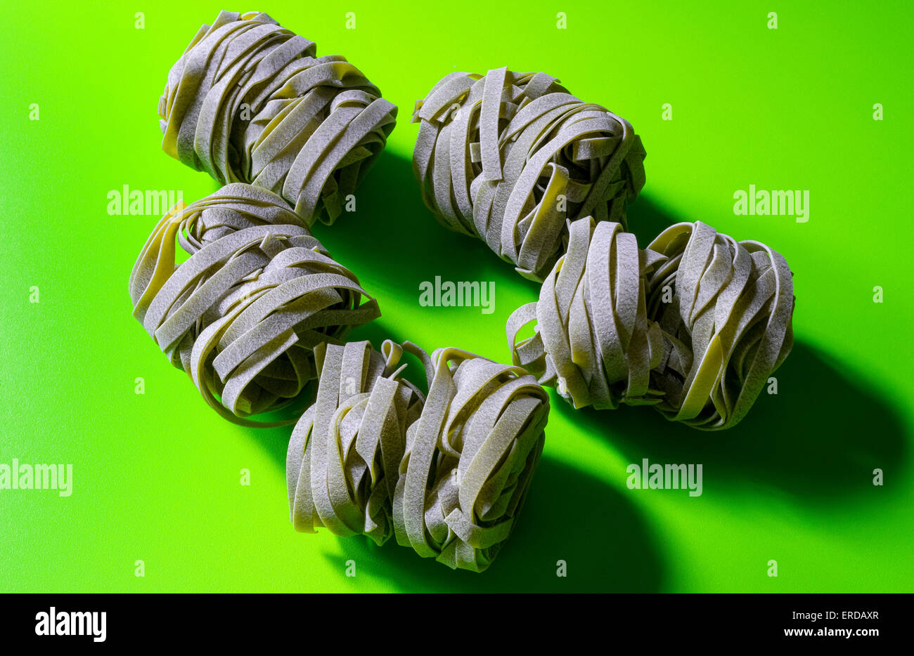 Wrapped portions of dry spinach fettuccine on a green table Stock Photo
