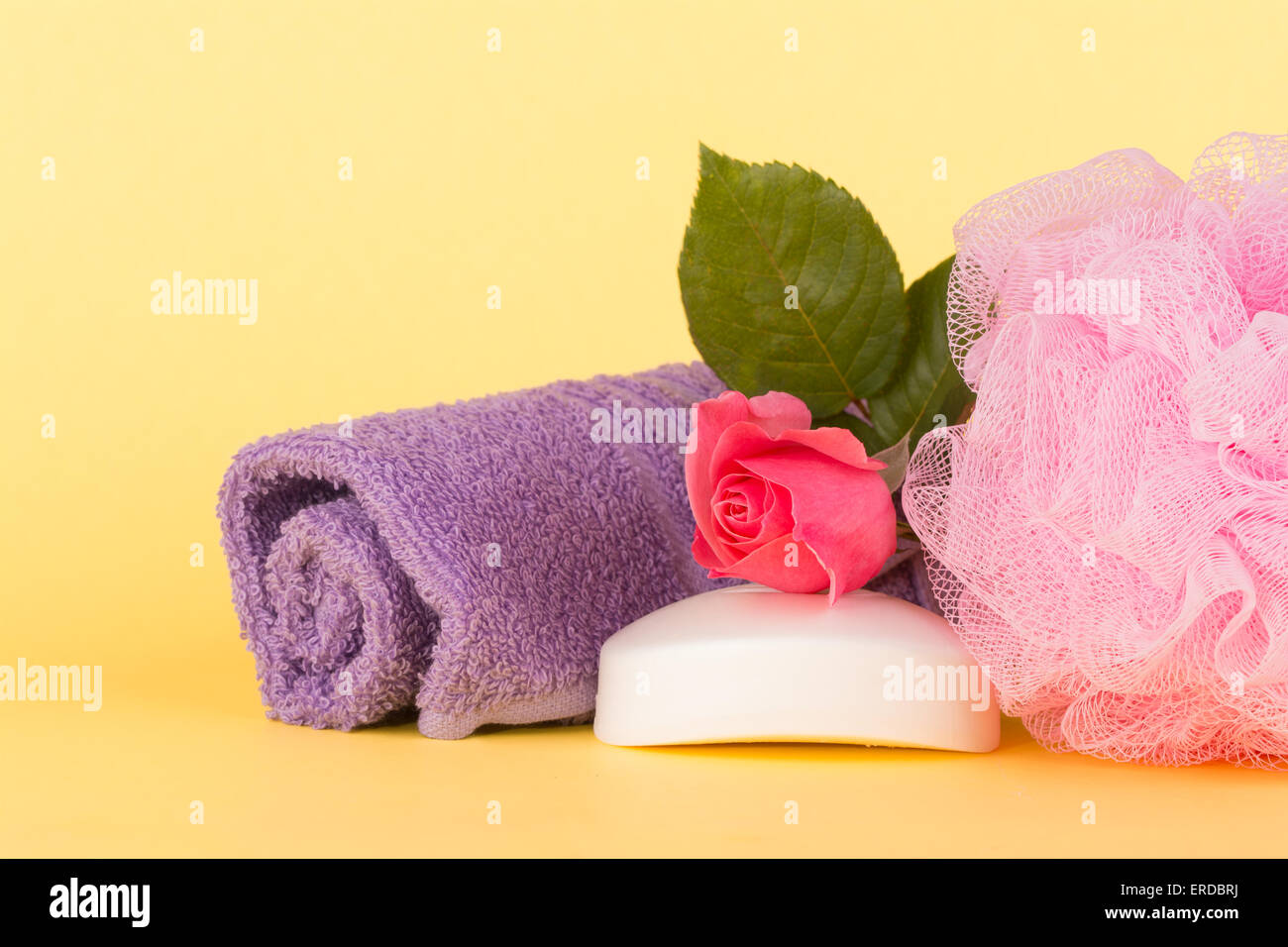 Soap topped with pink rose next to a shower puff and wash cloth against light yellow background Stock Photo