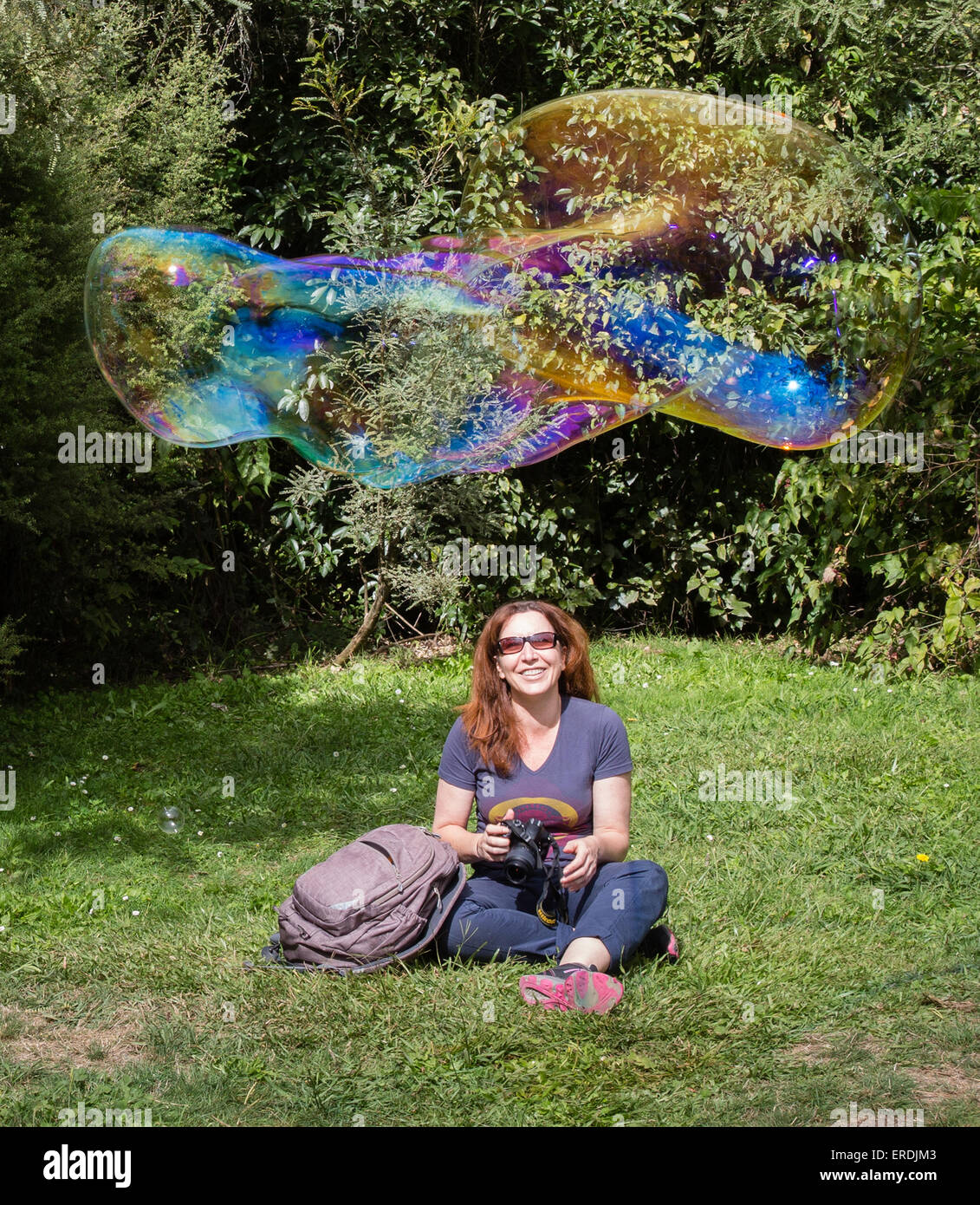 A happy smiling woman with a camera watches a newly formed giant soap bubble float past her Stock Photo