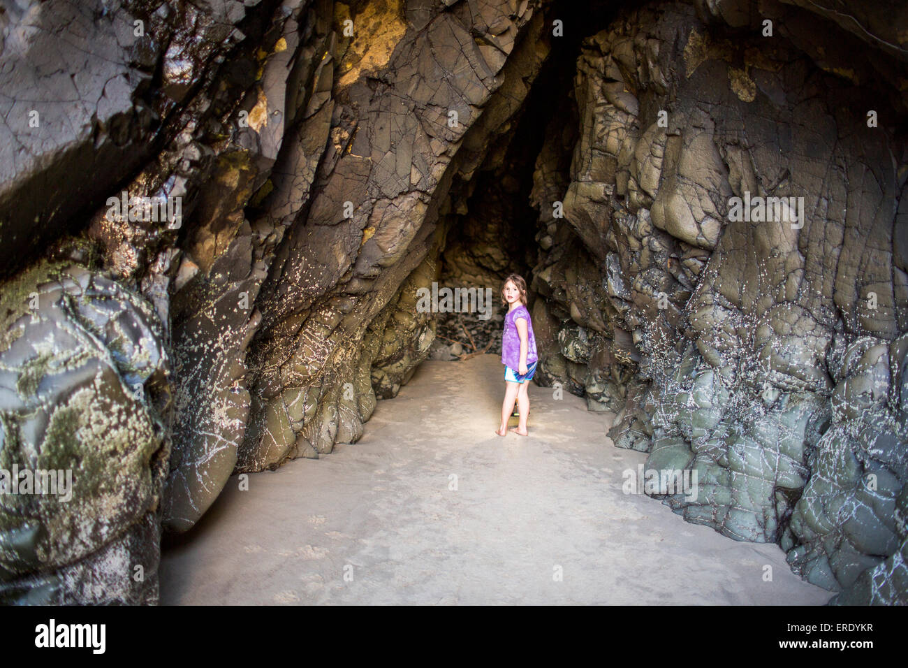 Caucasian girl exploring cave at beach Stock Photo