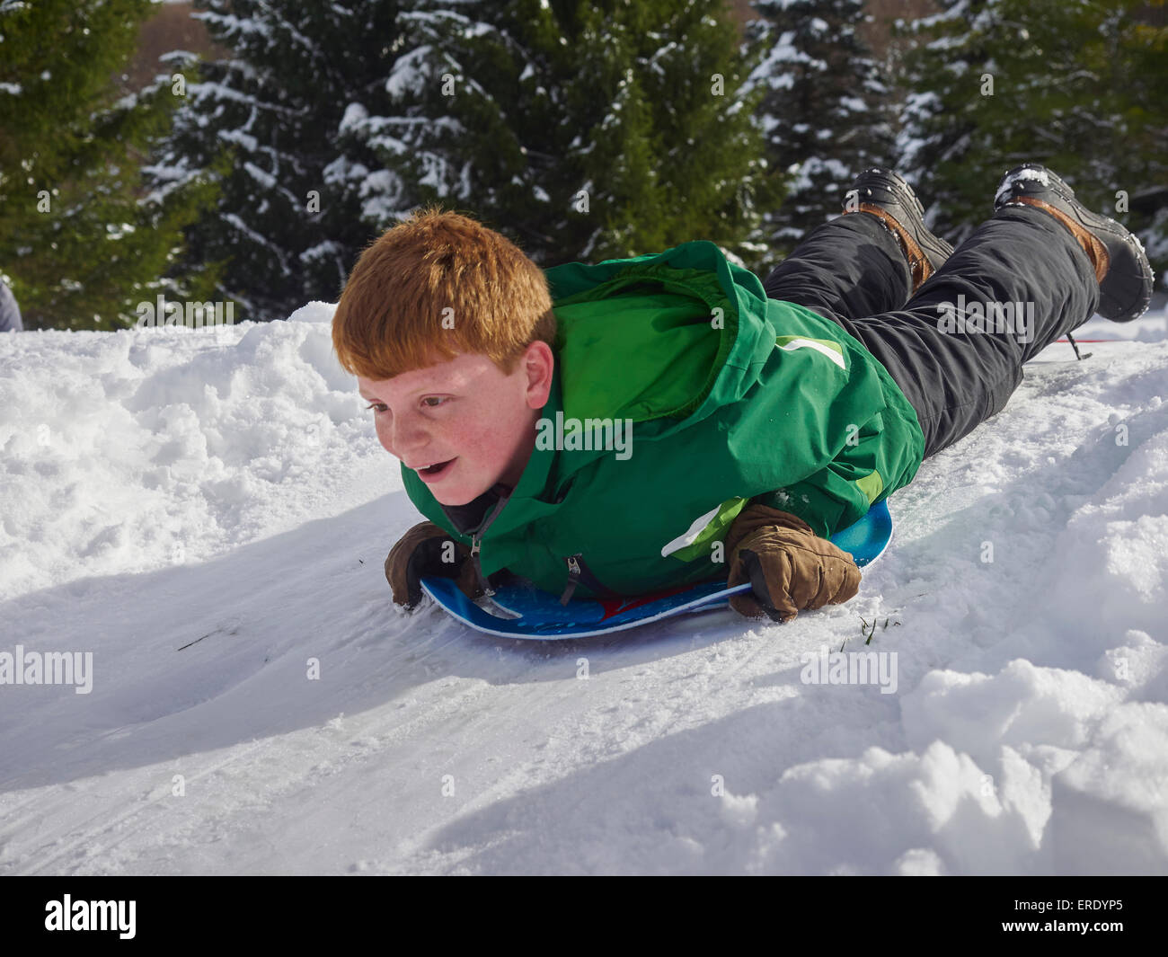 Caucasian boy sledding on snowy hill Stock Photo
