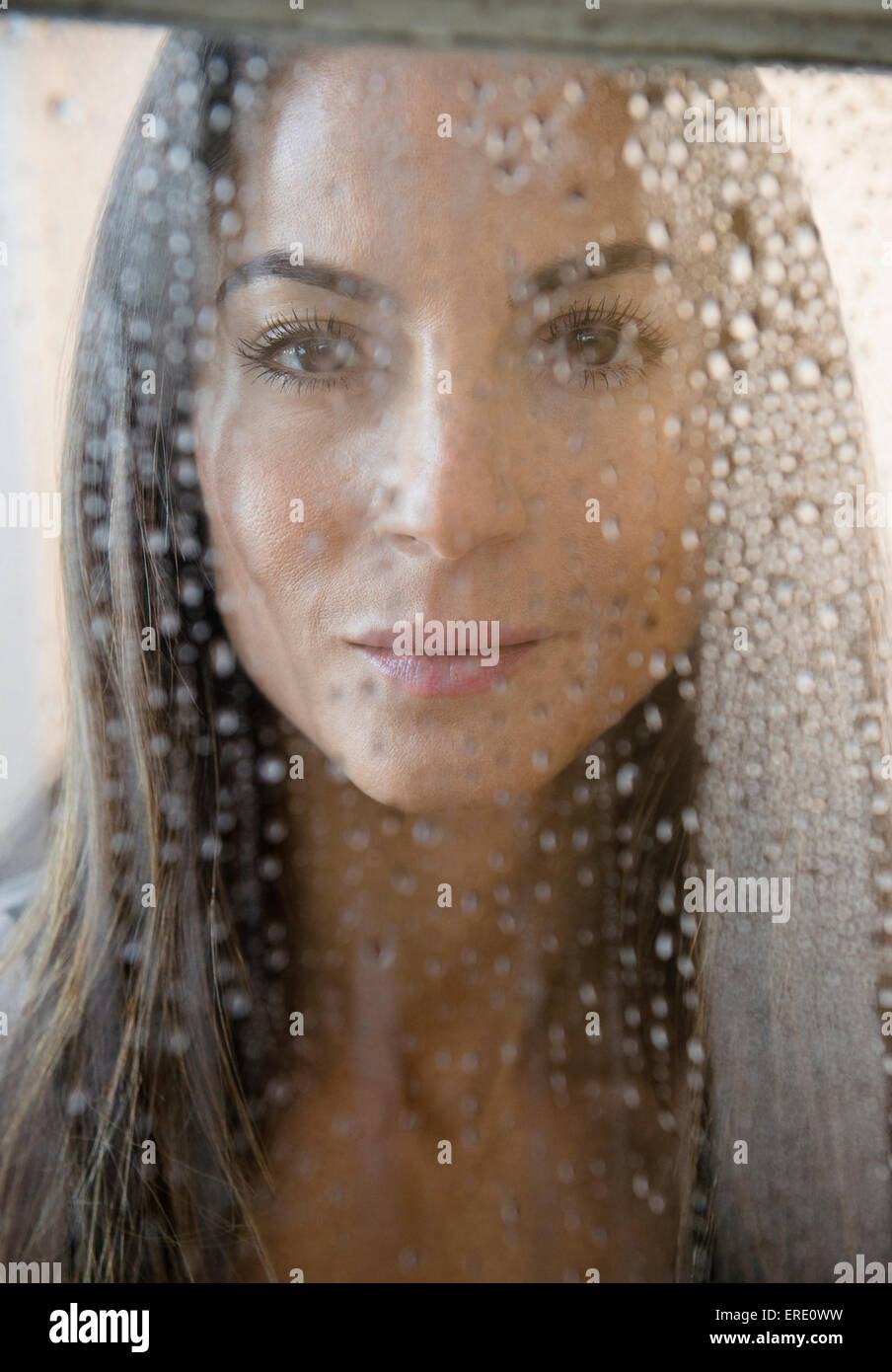 Caucasian woman peering through wet window Stock Photo