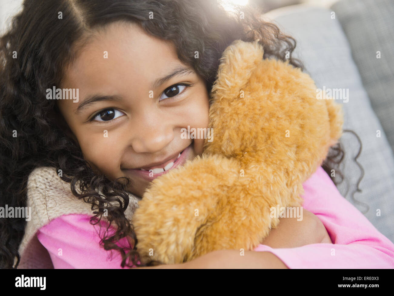 Mixed race girl hugging teddy bear on sofa Stock Photo