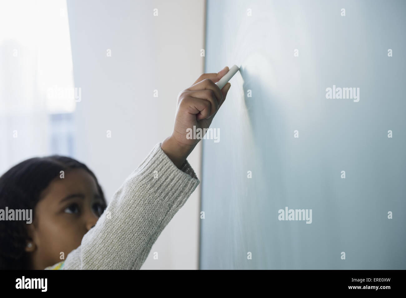 Mixed race student writing on chalkboard in classroom Stock Photo