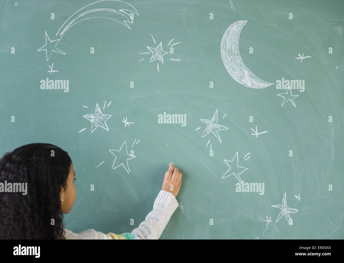 Mixed race student drawing stars on chalkboard in classroom Stock Photo