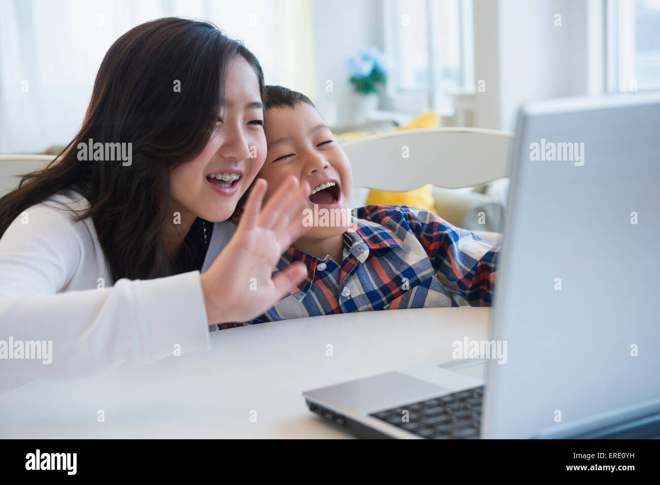 Brother and sister waving at video chat on computer Stock Photo