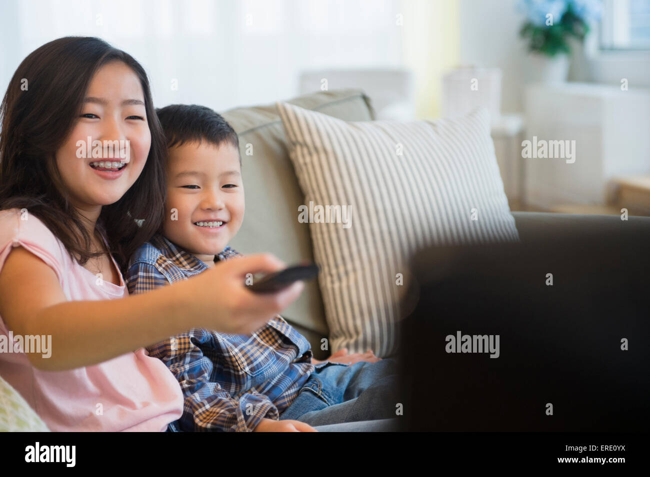 Asian brother and sister watching television on sofa Stock Photo