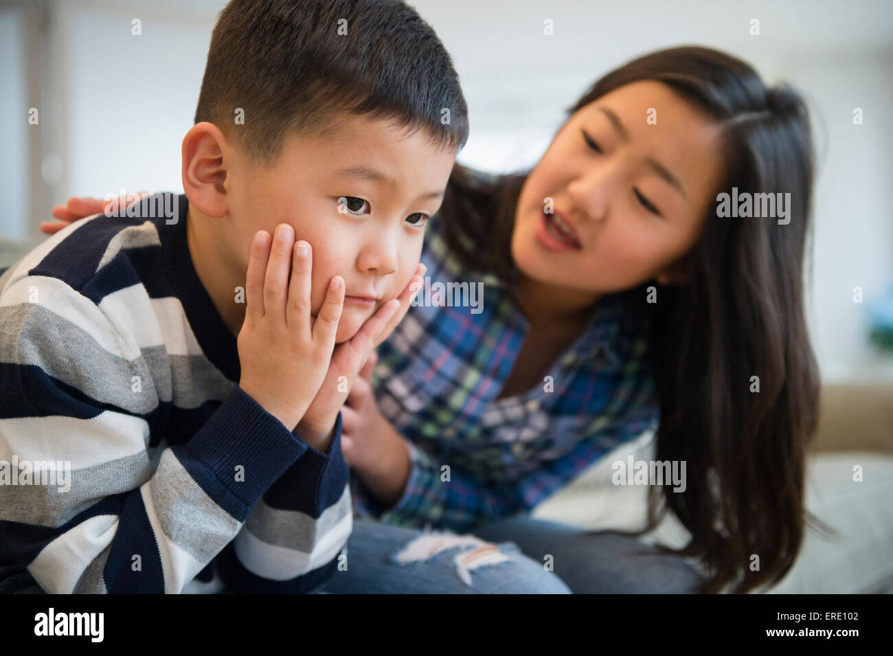 Asian sister comforting sad brother on sofa Stock Photo