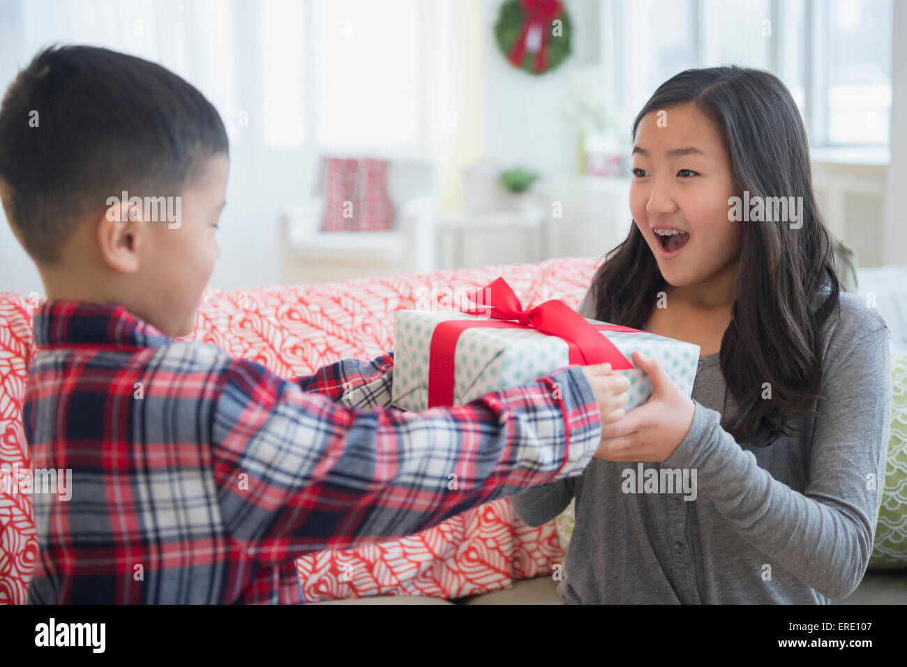 Asian brother giving sister Christmas gift in living room Stock Photo