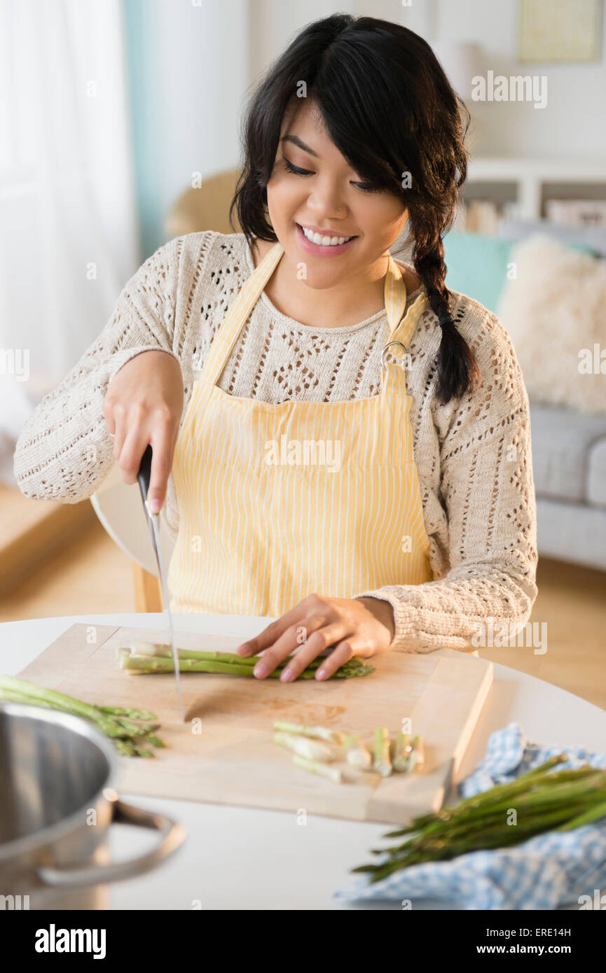 Pacific Islander woman slicing vegetables in kitchen Stock Photo