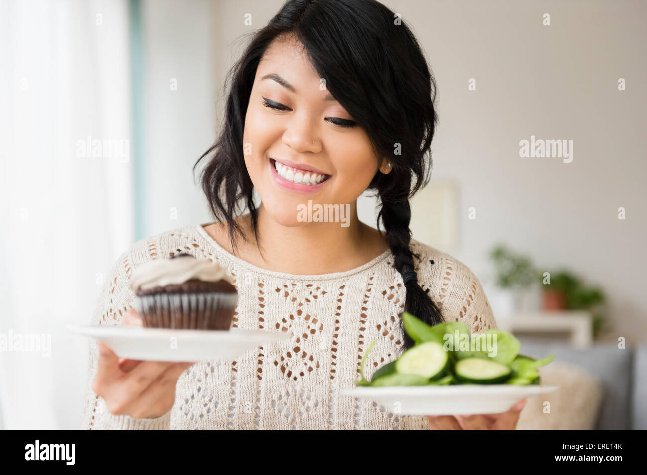 Pacific Islander woman choosing between cupcake and salad Stock Photo
