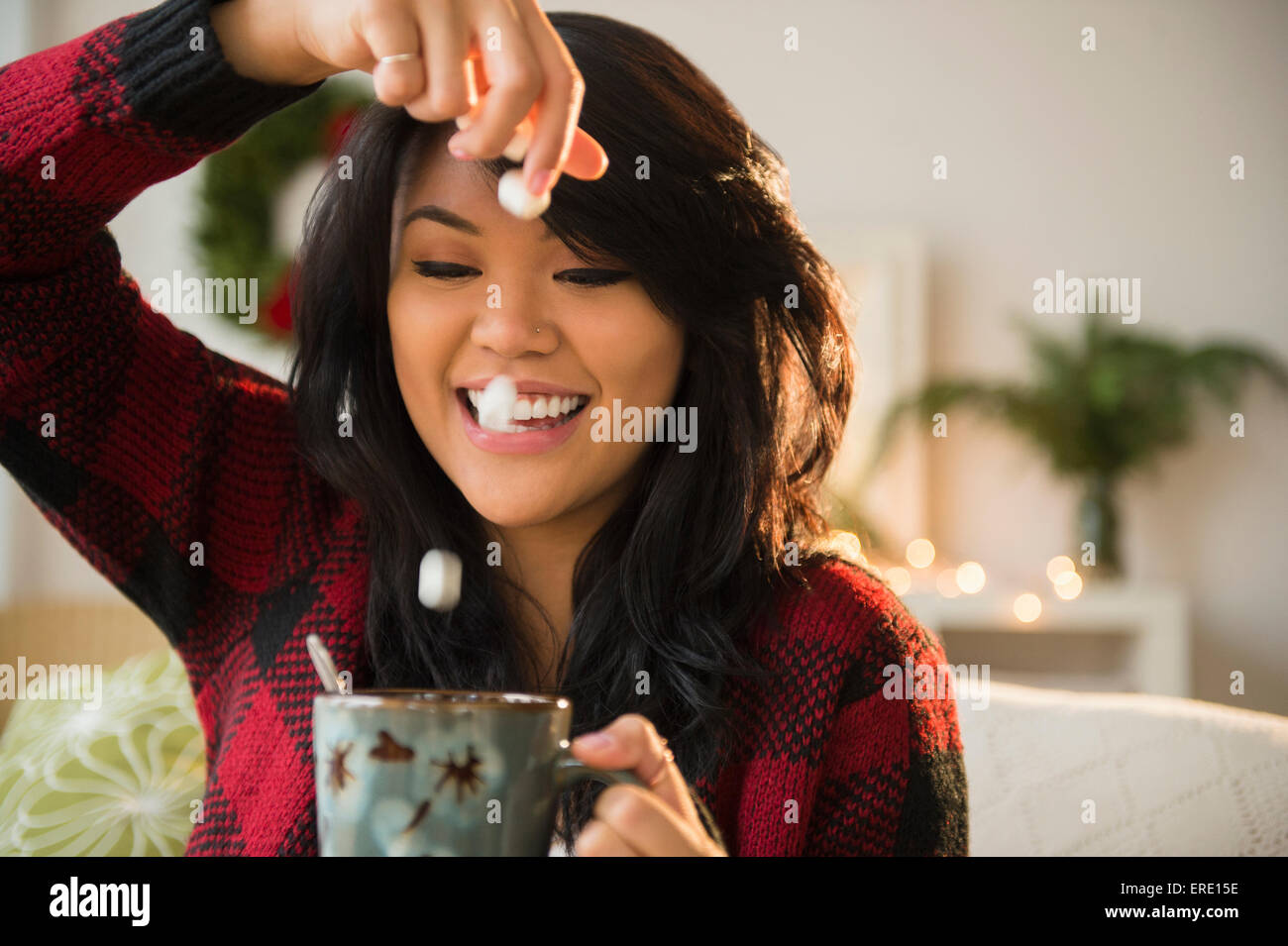 Pacific Islander woman dropping marshmallows into hot chocolate Stock Photo