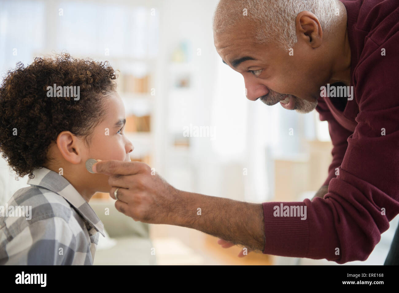 Mixed race grandfather pulling magic coin from ear of grandson Stock Photo