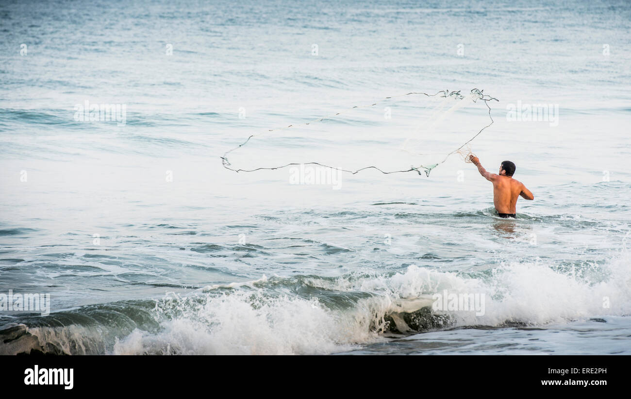 Man throwing fishing net into ocean waves Stock Photo