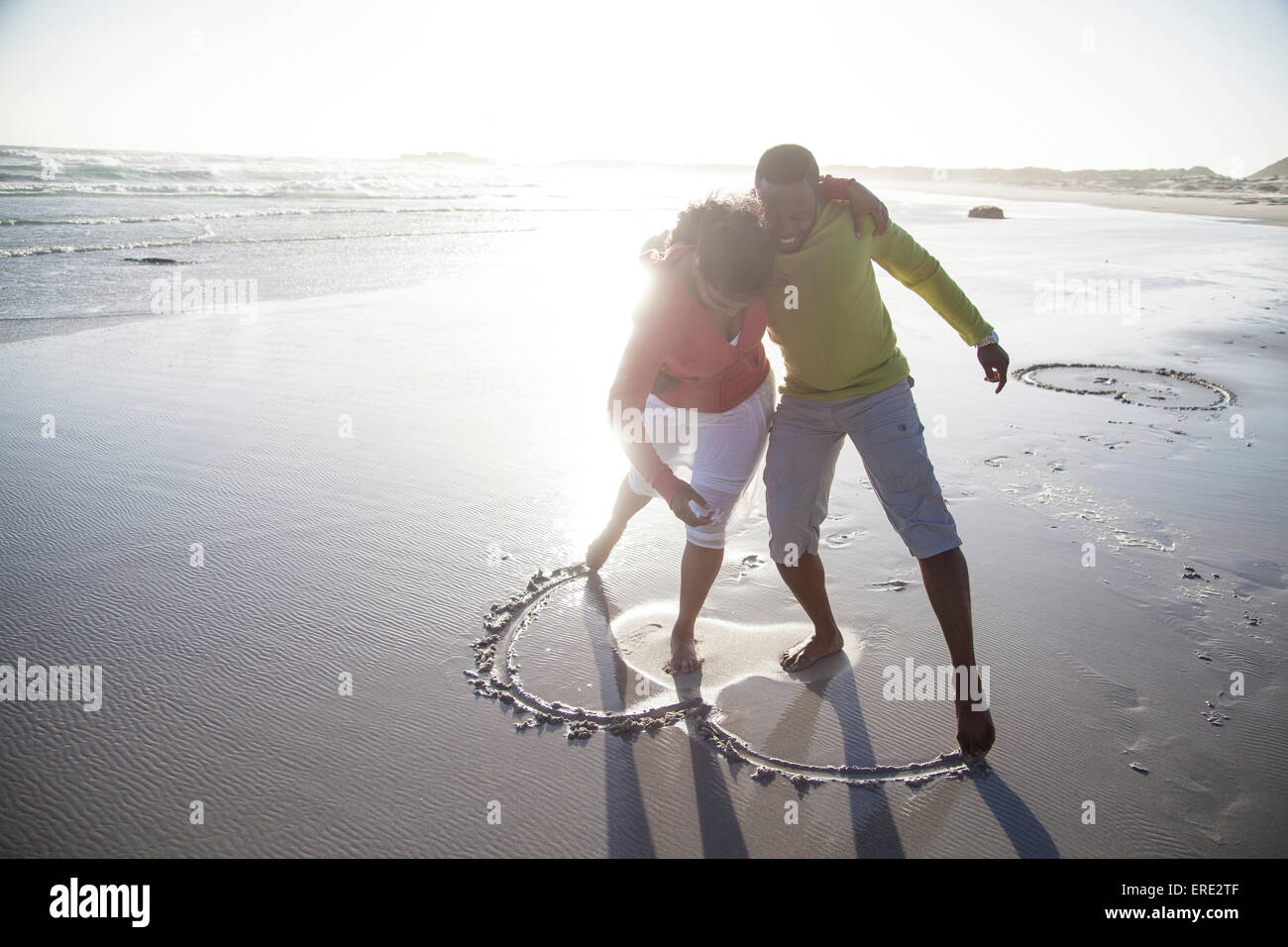 Couple drawing heart in sand on beach Stock Photo