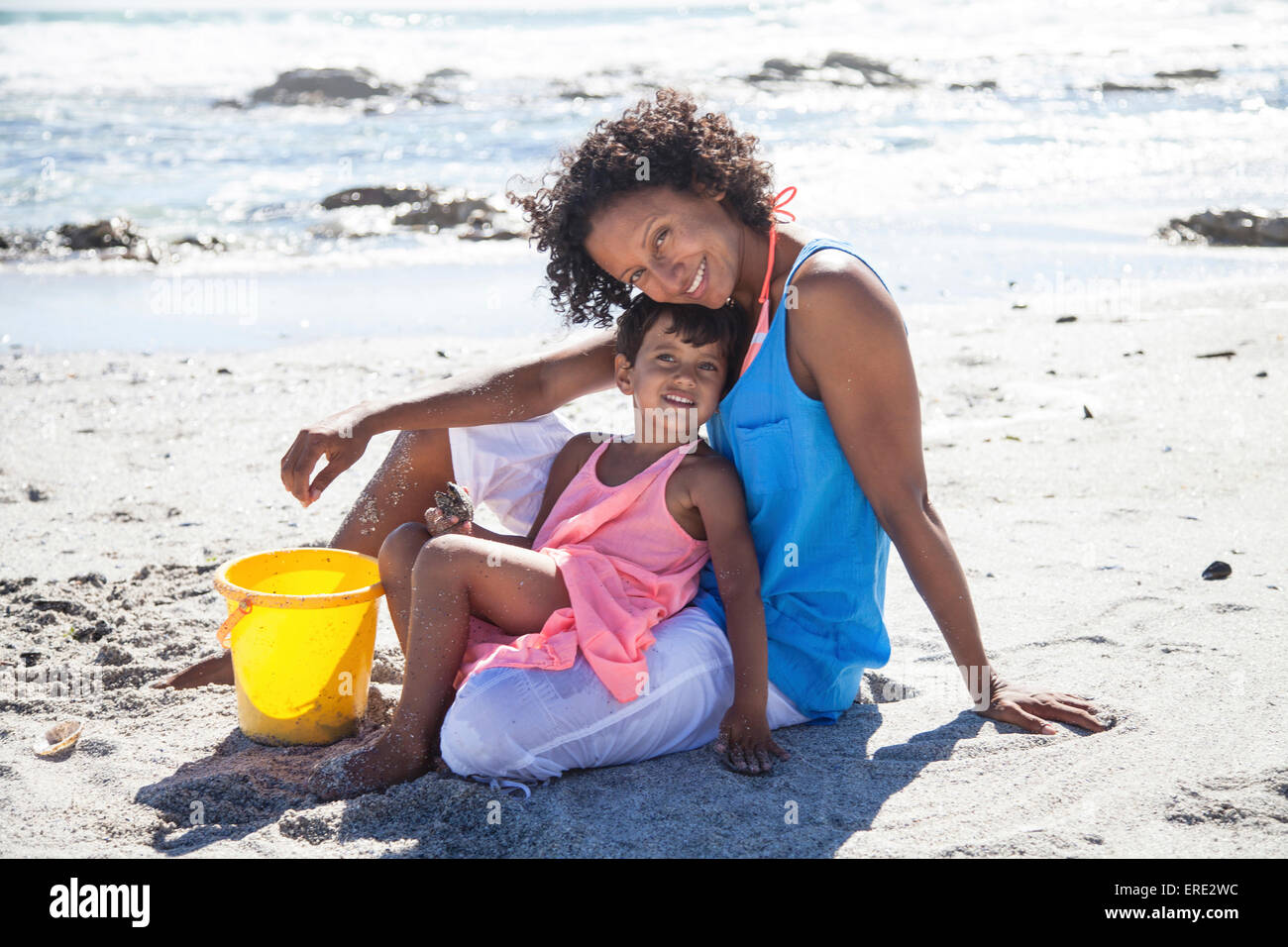 Mixed race mother and daughter sitting on beach Stock Photo