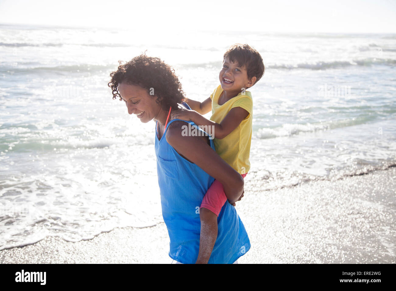 Mixed race mother carrying daughter piggyback on beach Stock Photo