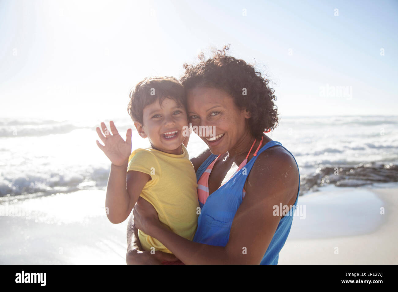 Mixed race mother and daughter waving on beach Stock Photo