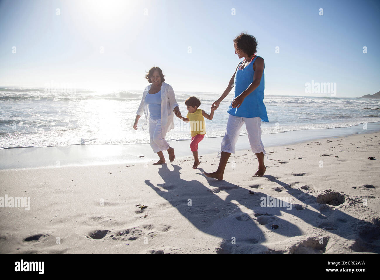 Mixed race grandmother, daughter and granddaughter walking on beach Stock Photo